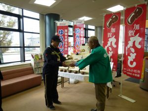 丸いもを郵便配達員に手渡す松本部会長